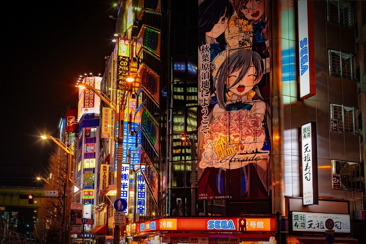 Panneau publicitaire lumineux affichant un manga, avec des néons colorés et l'animation caractéristique de Tokyo la nuit