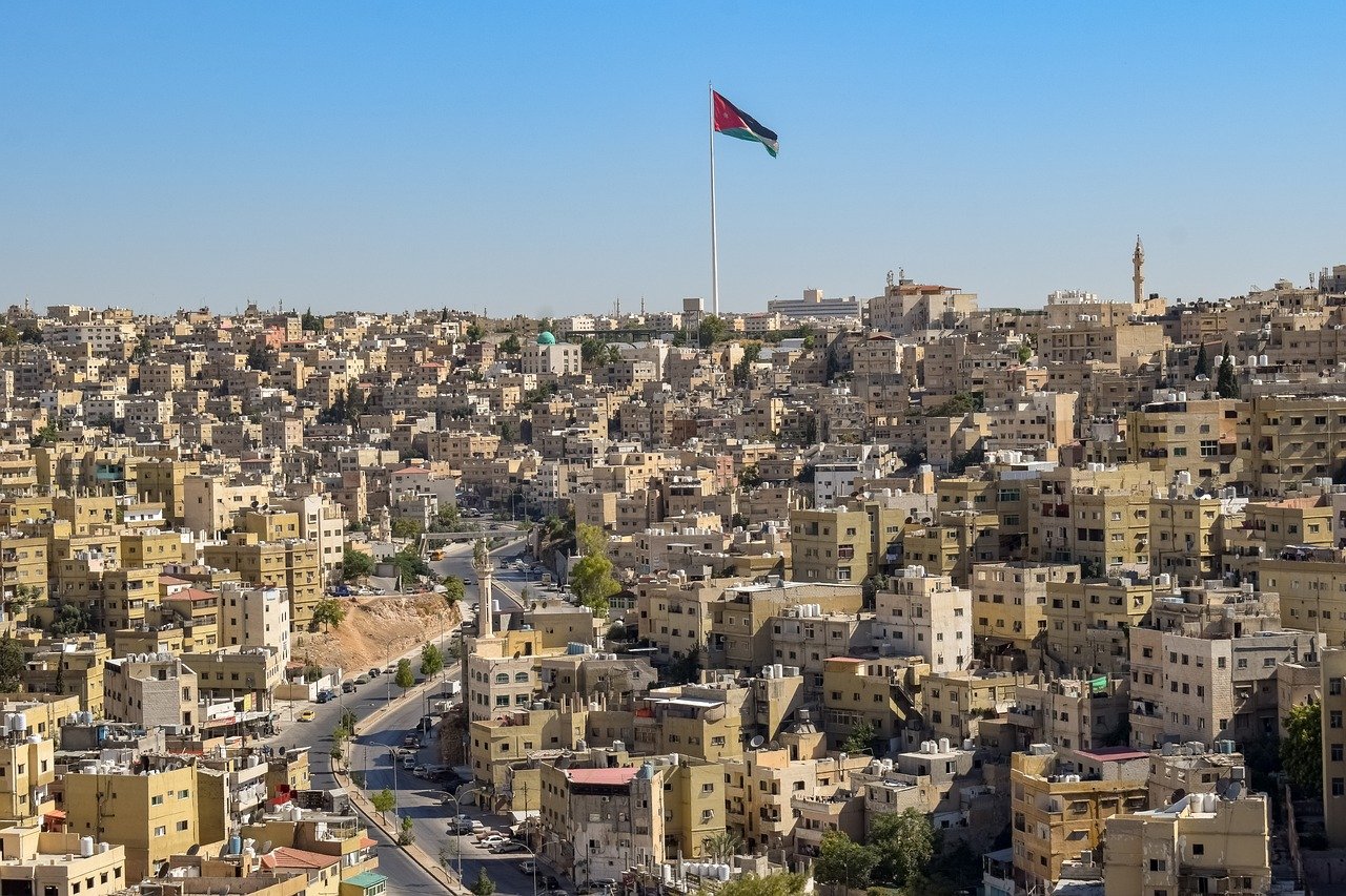 Vue panoramique sur la ville d'Amman, Jordanie, avec un drapeau jordanien flottant majestueusement au centre, entouré d'immeubles et de collines