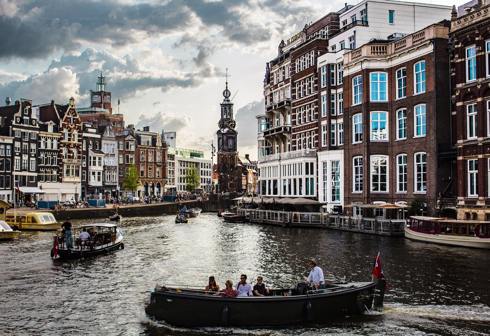 Vue sur l'Amstel à Amsterdam avec plusieurs barques naviguant sur le fleuve, entouré de l’architecture typique et des ponts emblématiques de la ville