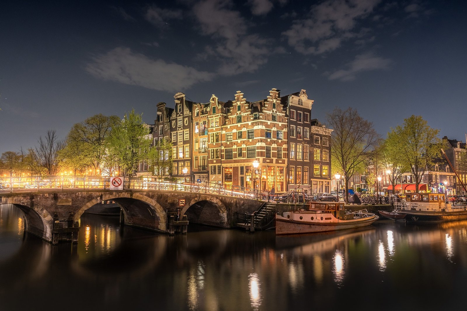 Vue sur l'Amstel à Amsterdam avec plusieurs barques amarrées sur le fleuve, entouré de l’architecture typique et des ponts emblématiques de la ville