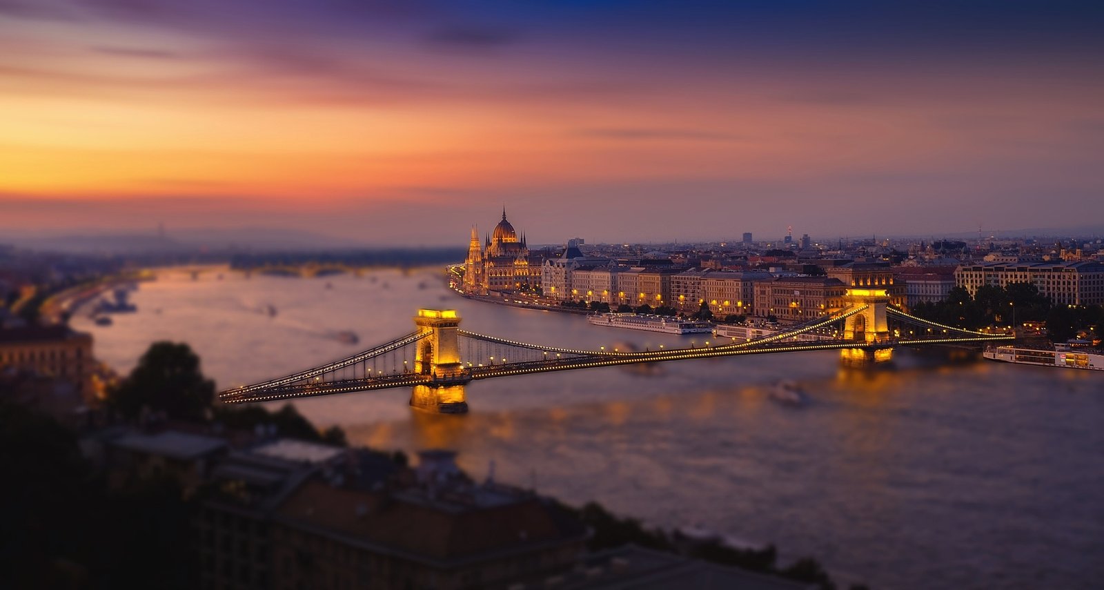 Vue aérienne de Budapest au coucher du soleil, mettant en lumière le Danube, le pont des Chaînes et le Parlement hongrois dans une ambiance dorée