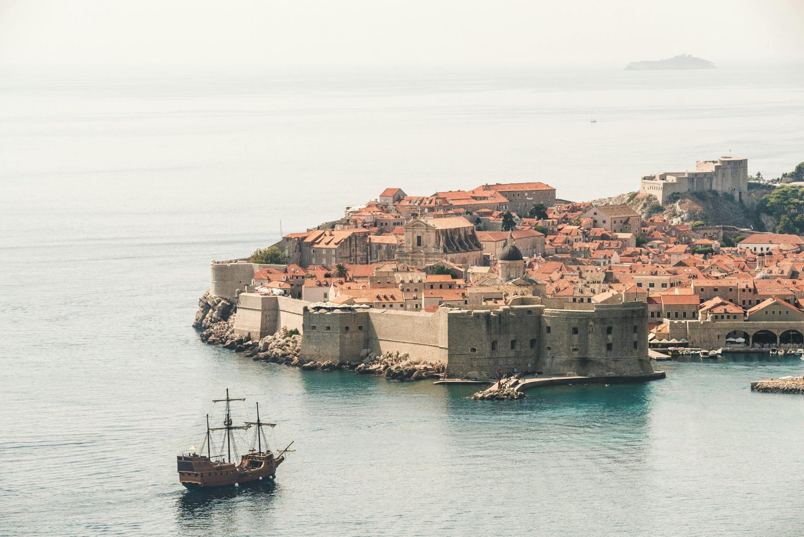 Vue de l'océan sur les remparts médiévaux de Dubrovnik, avec un bateau flottant paisiblement sur les eaux turquoise de la mer Adriatique