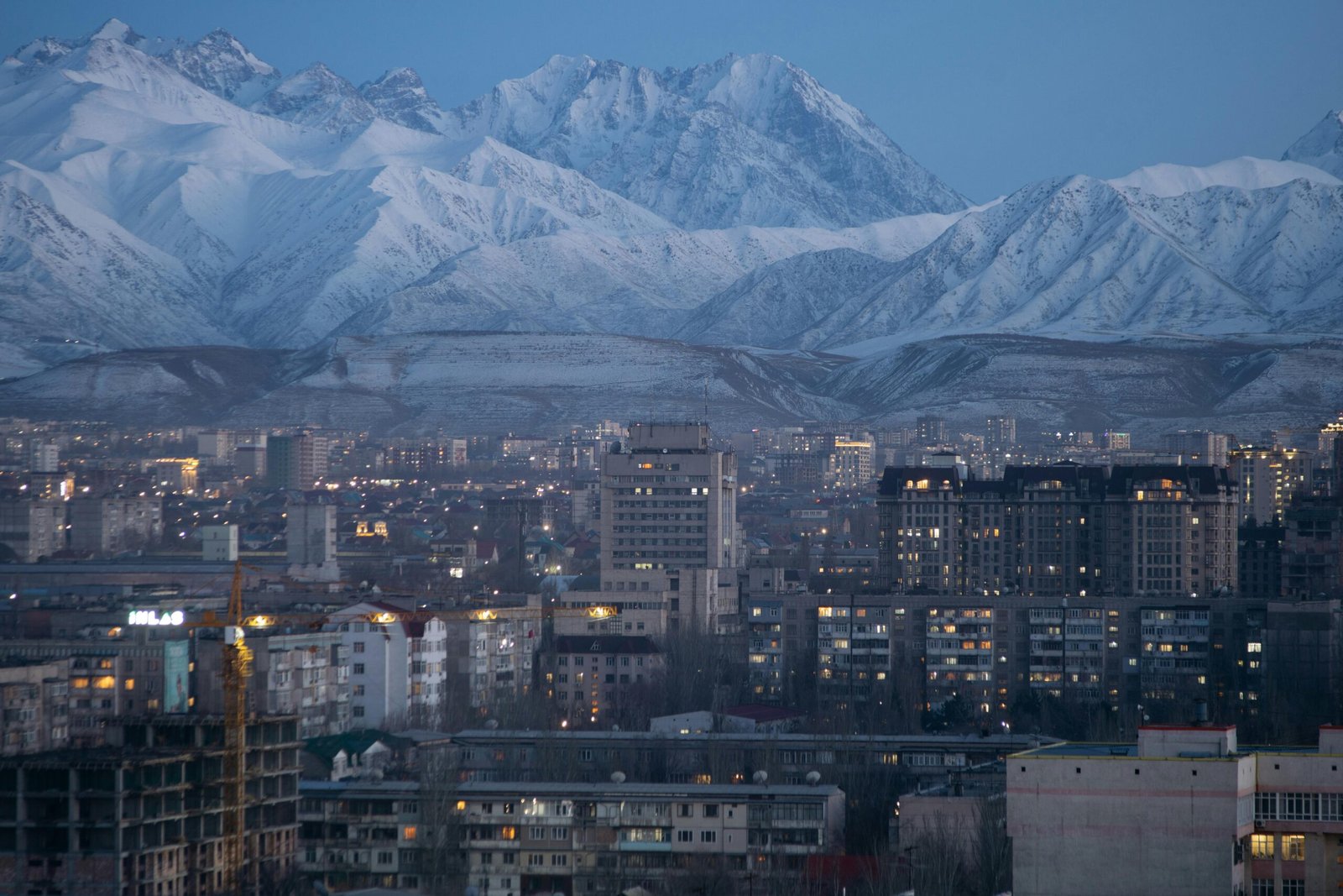 Vue panoramique du centre-ville de Bichkek au coucher du soleil avec une chaîne de montagnes en arrière-plan, offrant un contraste saisissant entre l'urbanisme et la nature kirghize