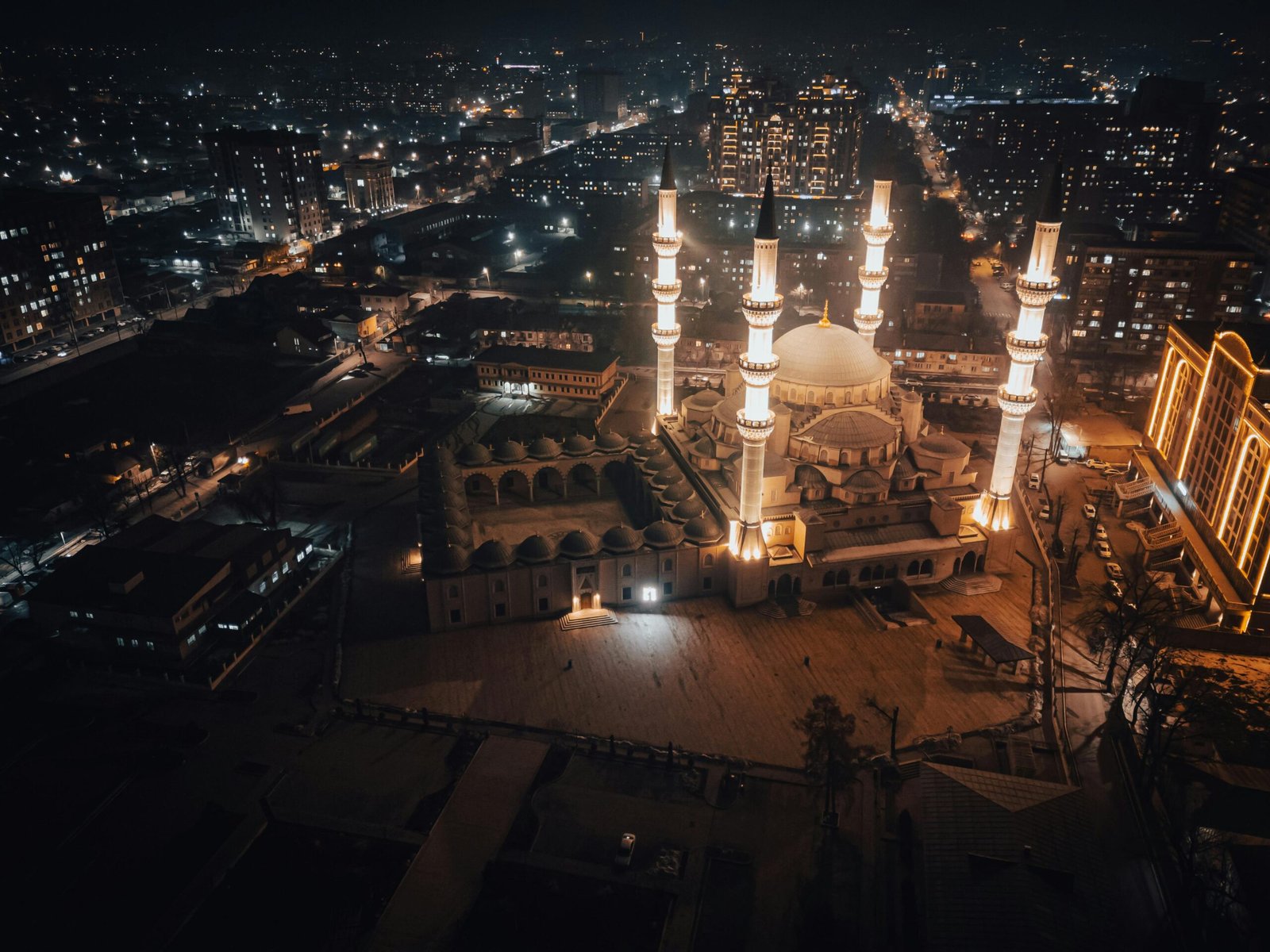 Vue aérienne d'une mosquée illuminée la nuit au Kirghizistan, avec la ville scintillante en arrière-plan, offrant un spectacle nocturne enchanteur