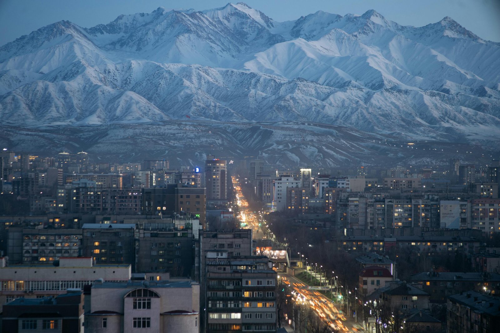 Vue panoramique du centre-ville de Bichkek au coucher du soleil avec une chaîne de montagnes en arrière-plan, offrant un contraste saisissant entre l'urbanisme et la nature kirghize