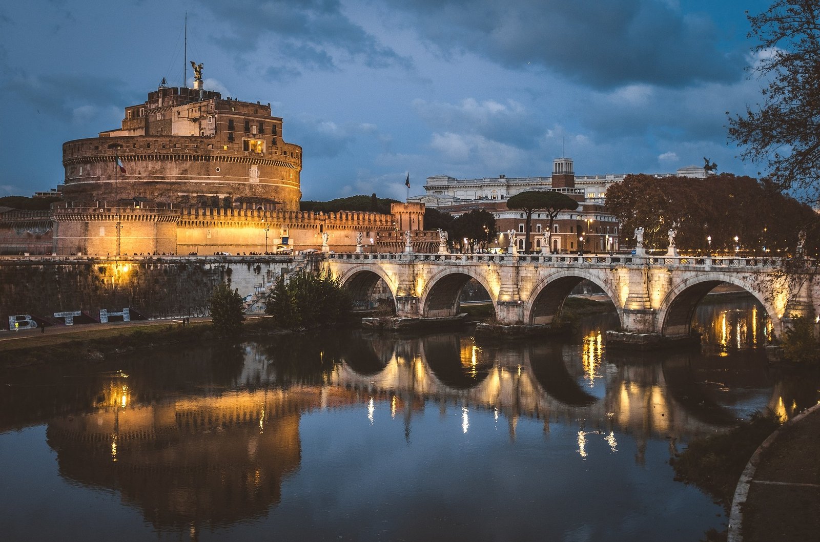 Vue sur le Pont Saint-Ange et le Château Saint-Ange à Rome, avec le pont illuminé et ses statues d'anges, reflétant son élégance dans le Tibre