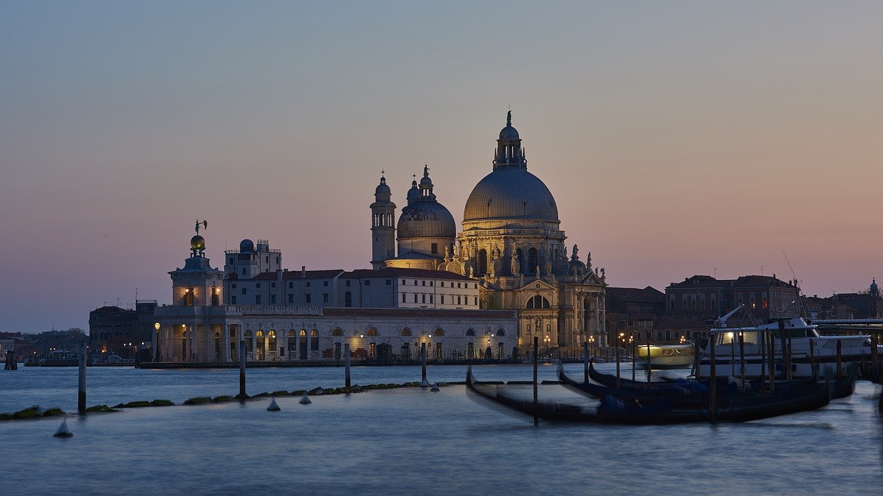 Basilique Saint-Marc, Venise, vue au coucher du soleil depuis un canal, avec des teintes dorées et des gondoles flottant sur l'eau