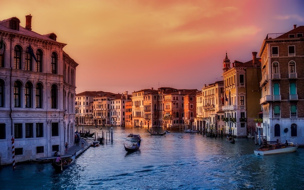 Photo du canal traversant Venise, bordé de bâtiments colorés et charmants, avec des barques amarrées et des gondoles naviguant paisiblement sur l'eau