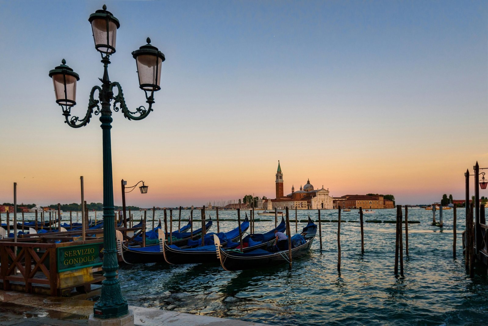 Vue lointaine sur Venise au coucher du soleil depuis un canal, avec des teintes dorées et des gondoles flottant sur l'eau