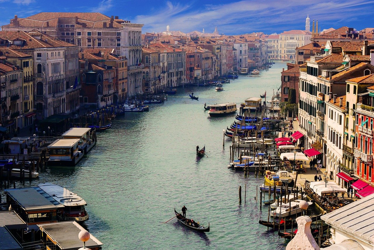 Photo du canal traversant Venise, bordé de bâtiments colorés et charmants, avec des barques amarrées et des gondoles naviguant paisiblement sur l'eau