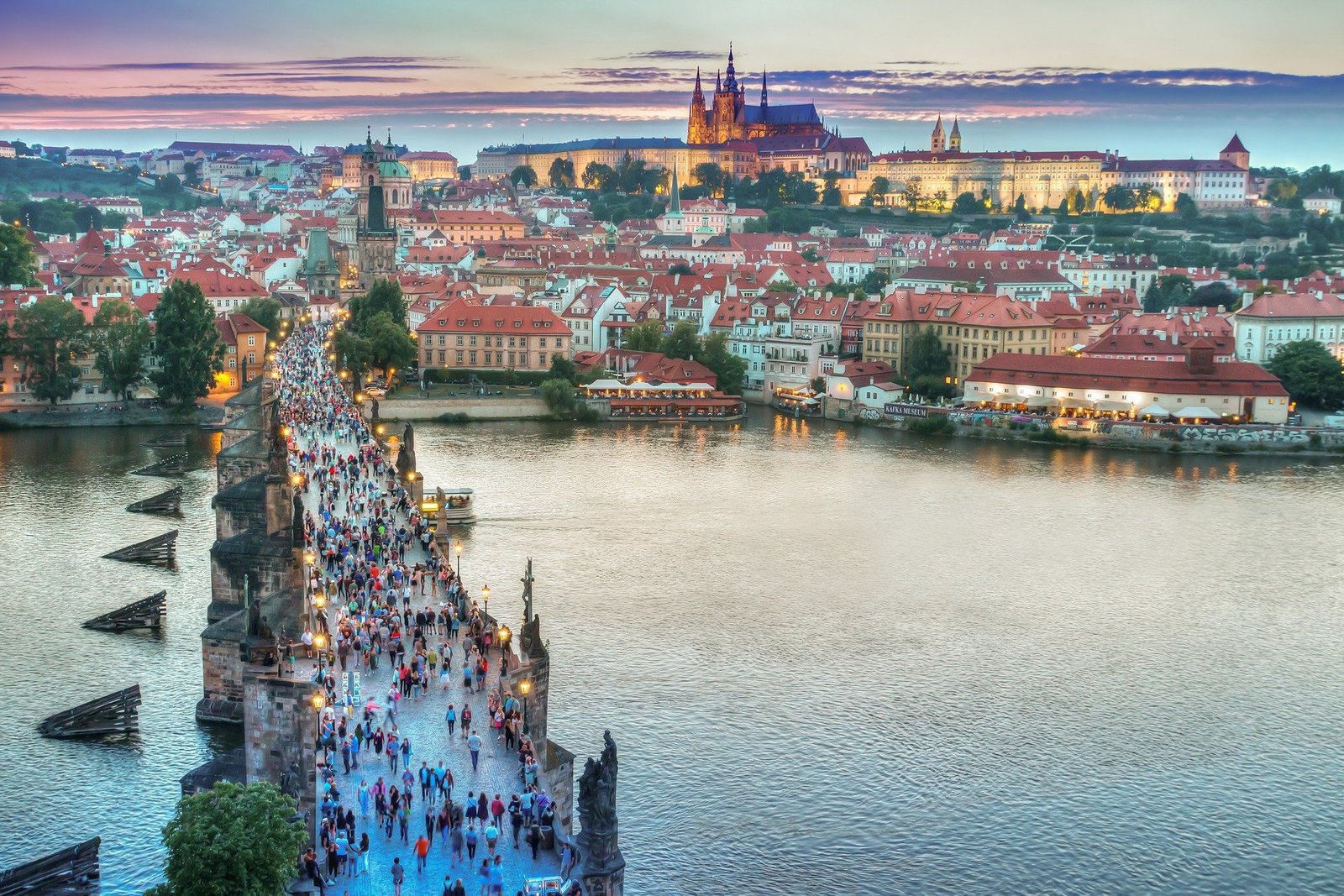 Vue panoramique sur la ville de Prague, en pleine journée avec le pont Charles en premier plan et le château de Prague en arrière-plan, offrant un paysage emblématique de la capitale tchèque