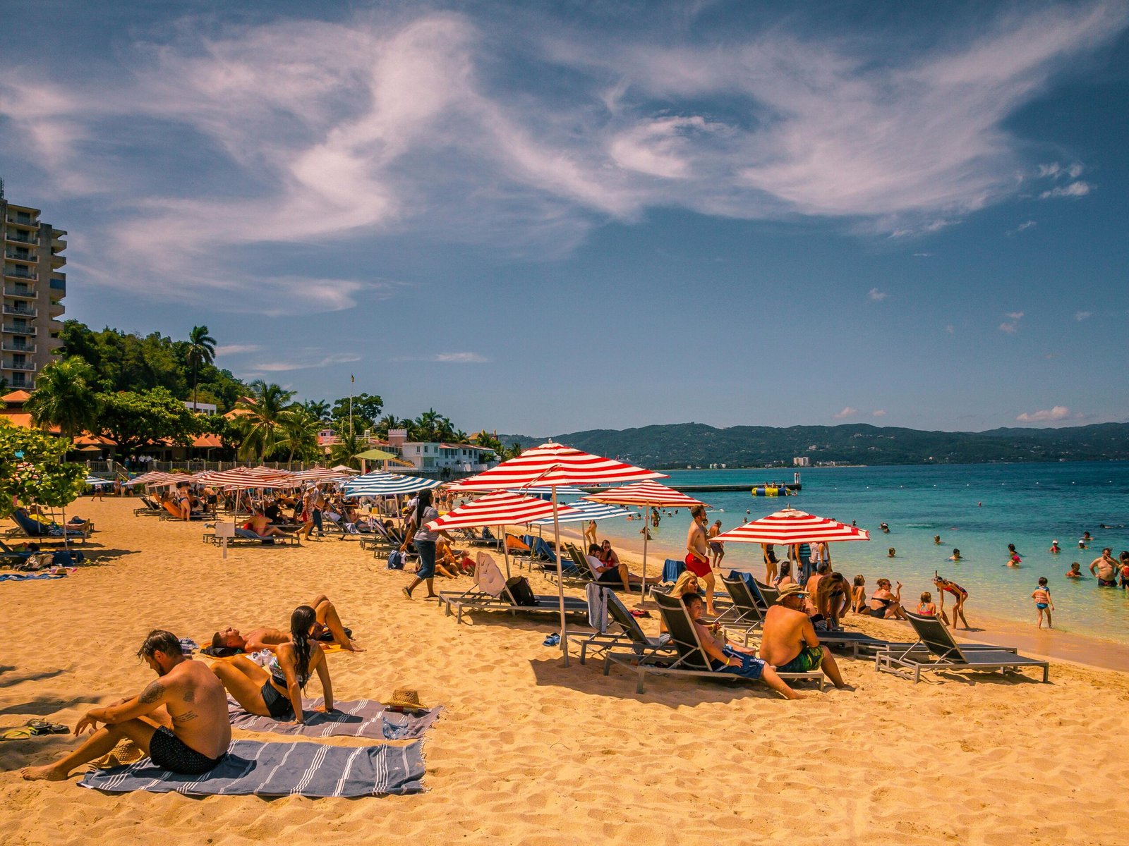 Plage animée en Jamaïque, avec des vacanciers profitant du sable doré, des eaux turquoise et de l’ambiance tropicale des Caraïbes