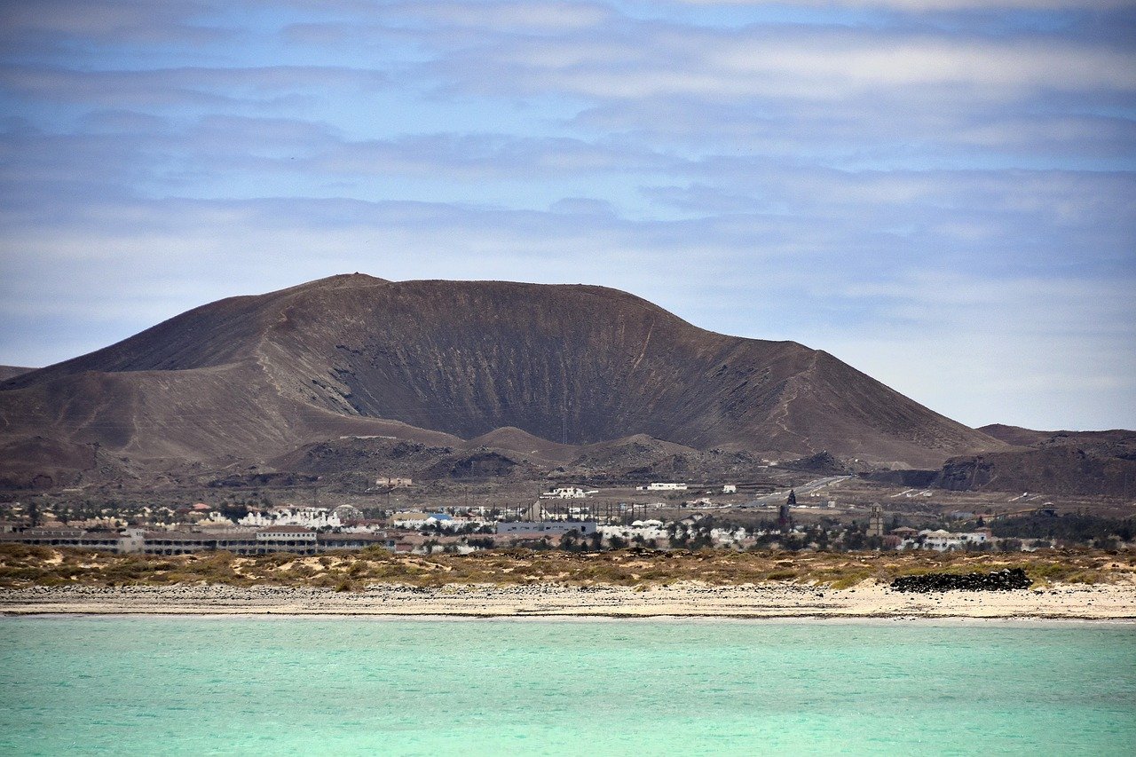Vue sur la mer bleue et un volcan emblématique de Fuerteventura, avec des paysages désertiques et un ciel ensoleillé en arrière-plan