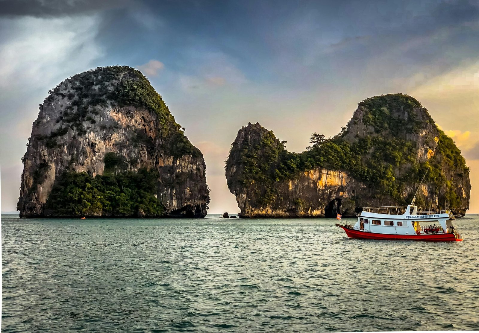 Bateau naviguant en pleine mer près de Phuket, avec la côte verdoyante et les formations rocheuses visibles à l’horizon sous un ciel clair