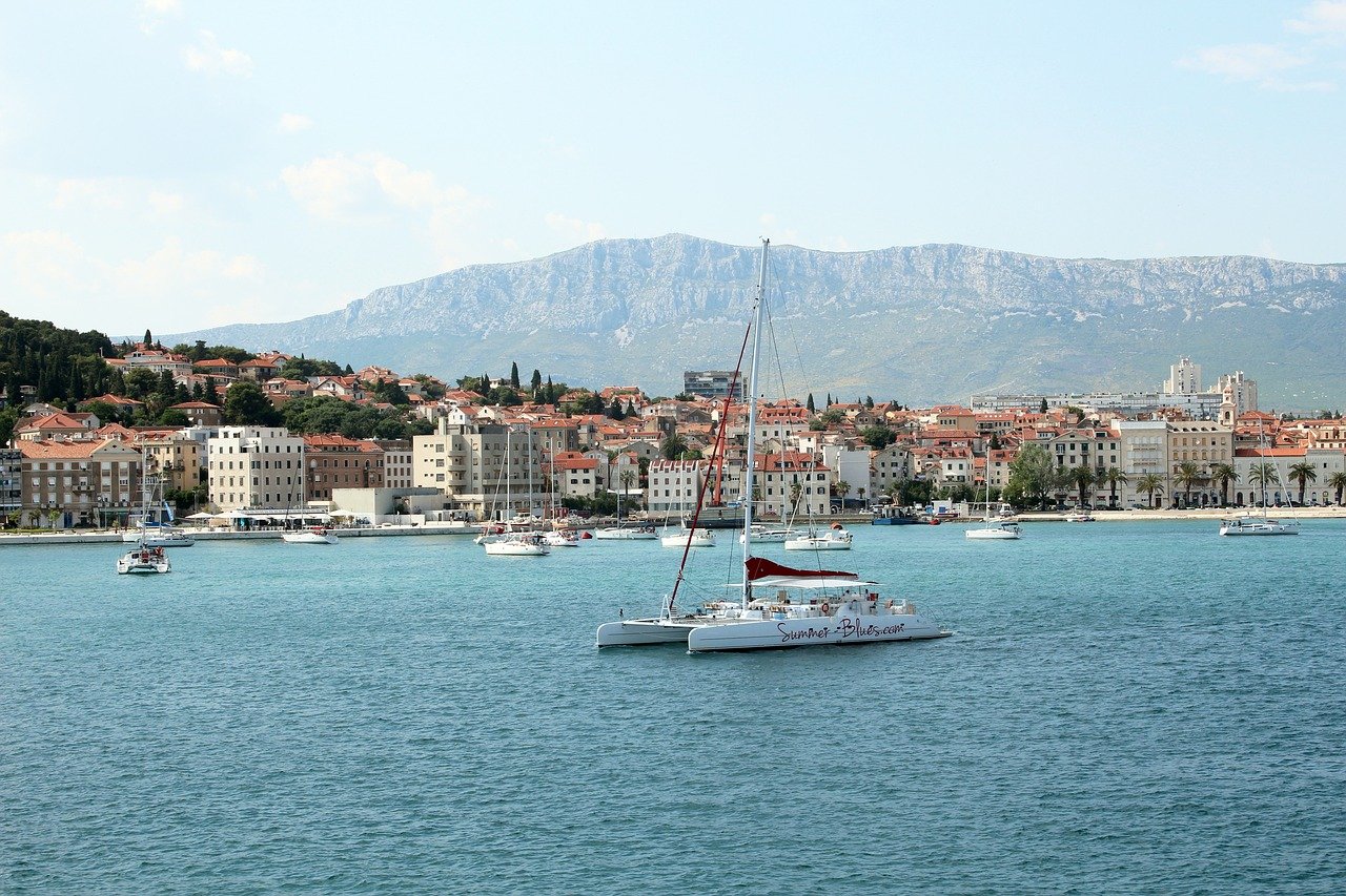 Bateau naviguant en pleine mer près de Split, avec la ville historique et ses bâtiments en arrière-plan, surplombés par des montagnes sous un ciel dégagé