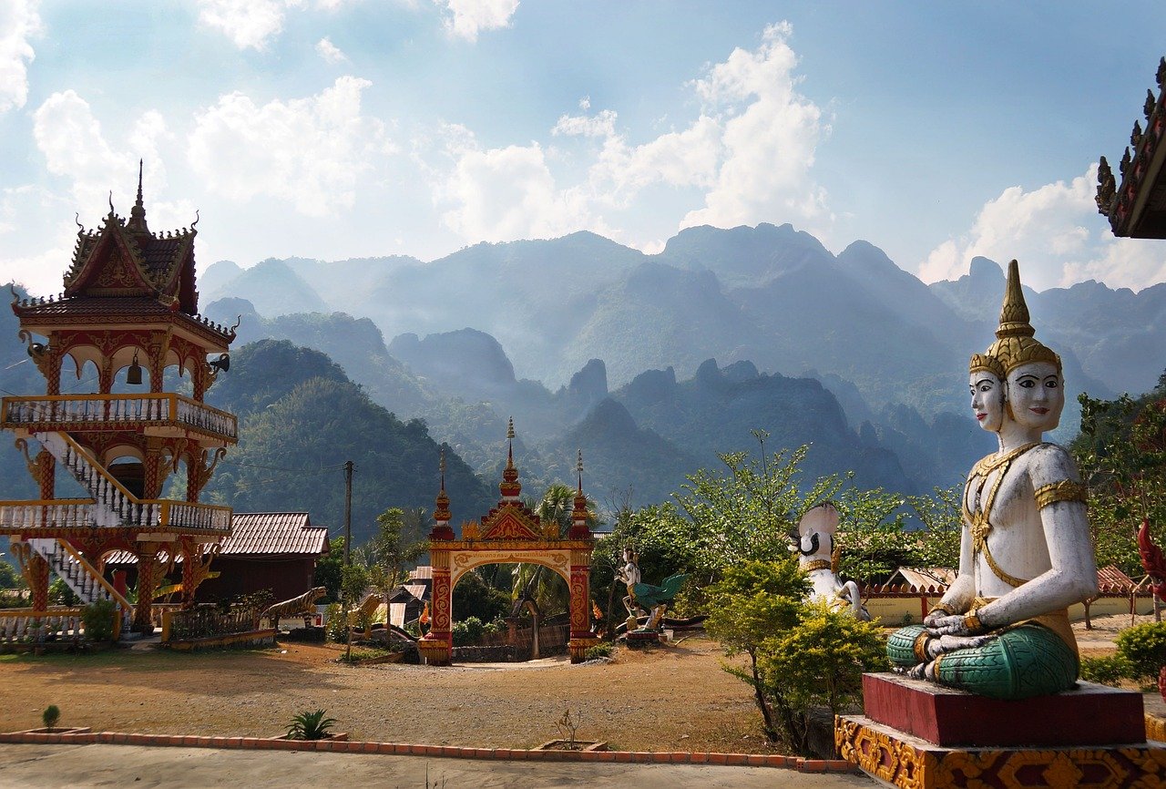 Temple traditionnel au Laos avec une montagne verdoyante en arrière-plan, sous un ciel bleu, illustrant la sérénité et la spiritualité du paysage