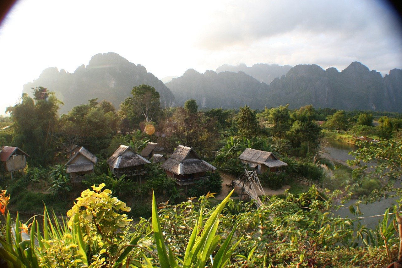 Paysage naturel au Laos avec des montagnes verdoyantes, des rizières en terrasses et des maisons traditionnelles en bois, offrant une scène rurale paisible et authentique