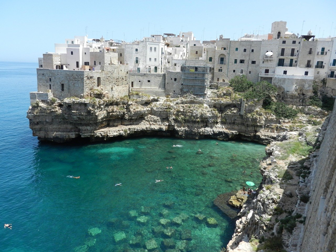 Maisons blanches traditionnelles surplombant une eau turquoise cristalline dans la région des Pouilles, en Italie, créant un contraste éclatant sous le soleil méditerranéen