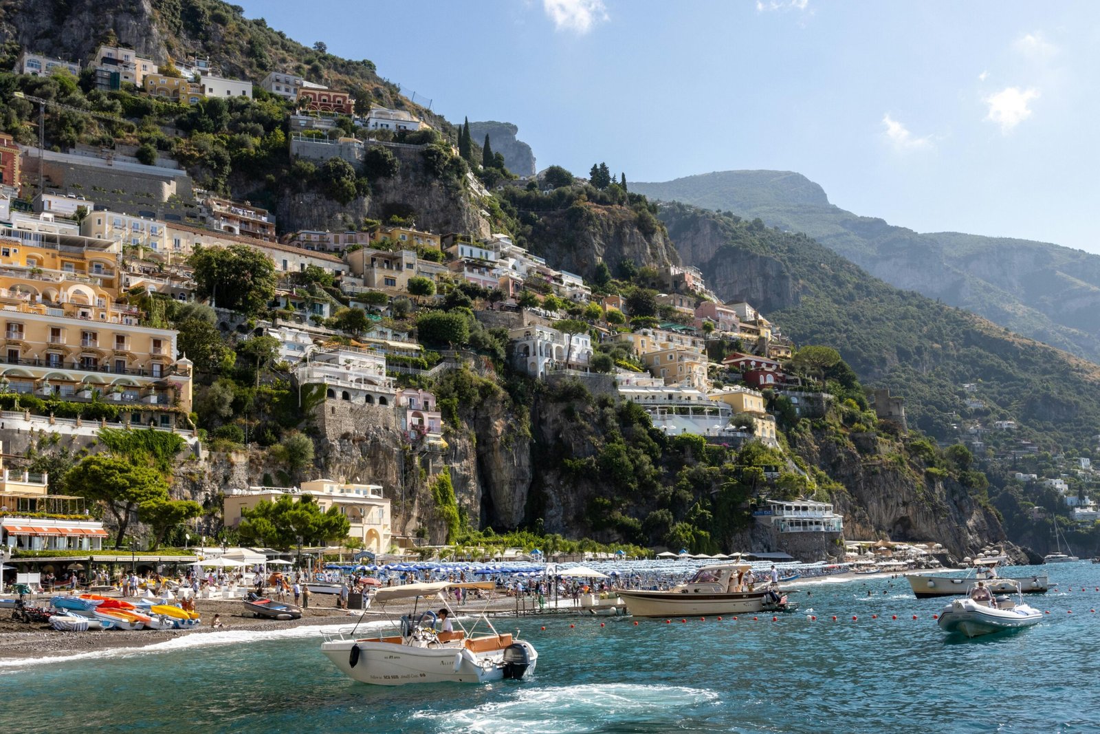 Vue sur Positano avec ses maisons colorées en terrasse, plage animée et bateaux amarrés sur la côte amalfitaine