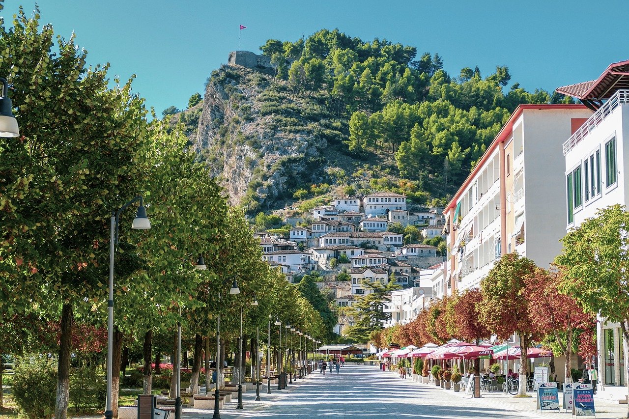 Village traditionnel niché dans les montagnes albanaises, avec des maisons en pierre aux toits rouges entourées de verdure luxuriante