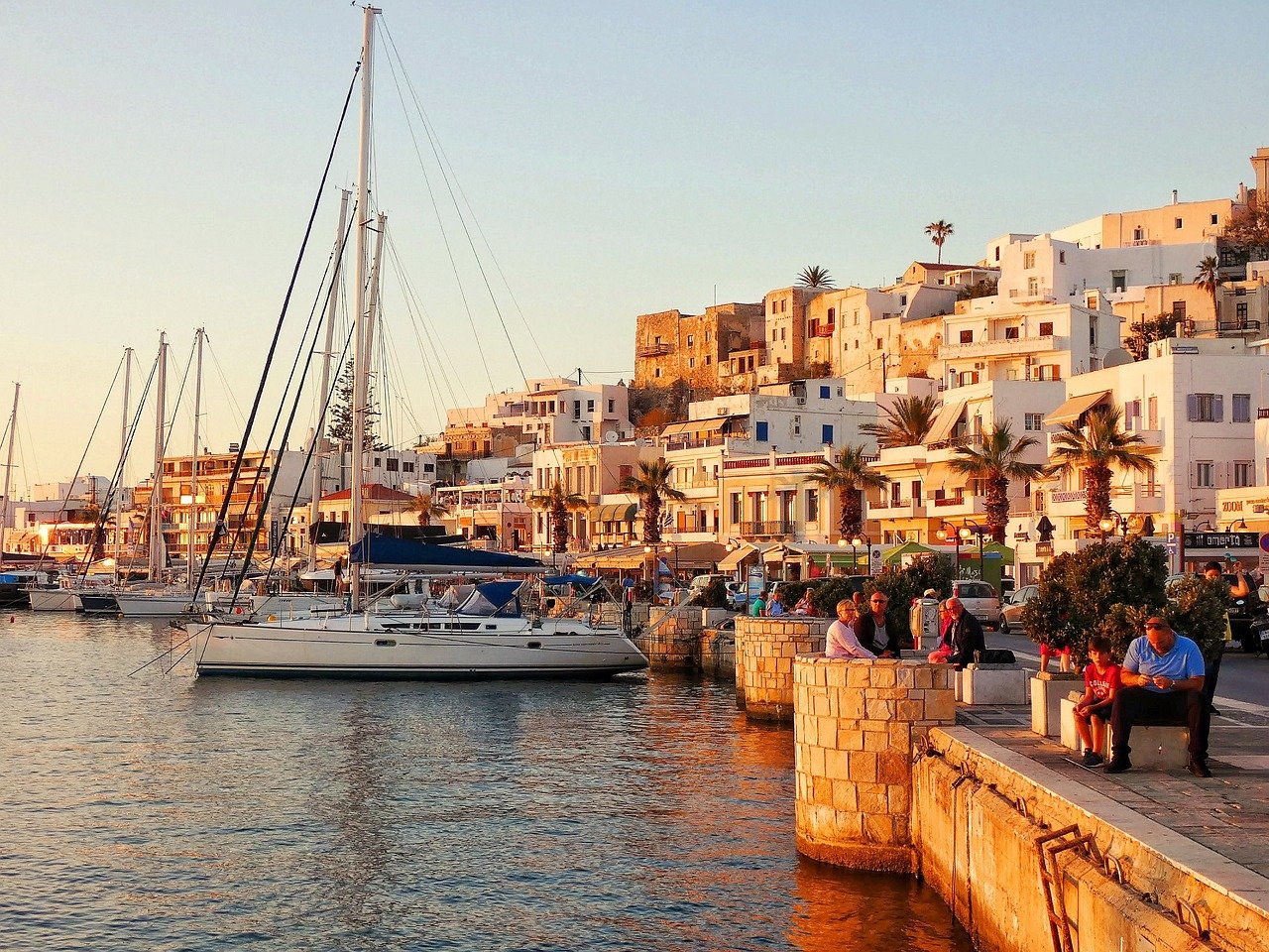 Port de Naxos en Grèce au coucher du soleil, avec des touristes qui se promènent et les maisons blanches typiques des Cyclades en arrière-plan